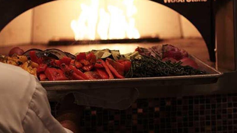 Tray of vegetables being placed in brick oven